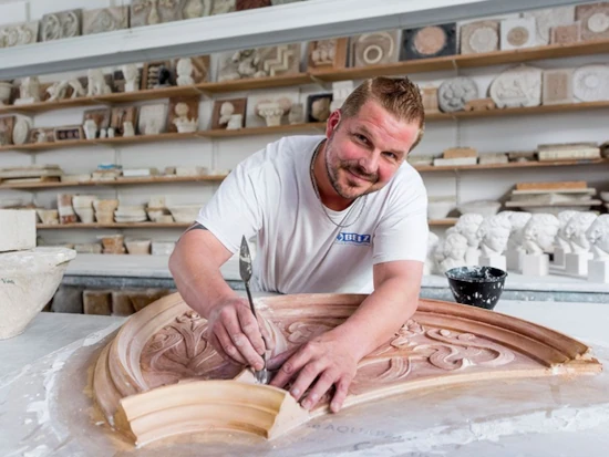 Ein Stuckateur bearbeitet kunstvolle Stuckornamente in einer Werkstatt für Stuckarbeiten.
