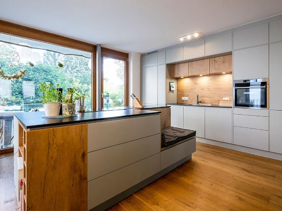 Moderne Einbauküche mit Kochinsel, Holzdetails, großen Fenstern und hellen Fronten.