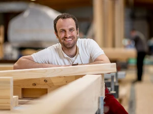 Lächelnder Handwerker in moderner Holzwerkstatt arbeitet an einem Holzprojekt.
