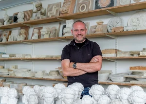 Ein Mann steht in einer Werkstatt mit vielen Gipsbüsten und Reliefs für Kunsthandwerk.