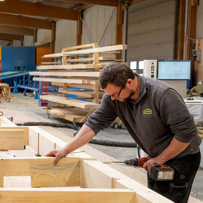 Ein Schreiner arbeitet in einer modernen Werkstatt mit Holz und einer Bohrmaschine.